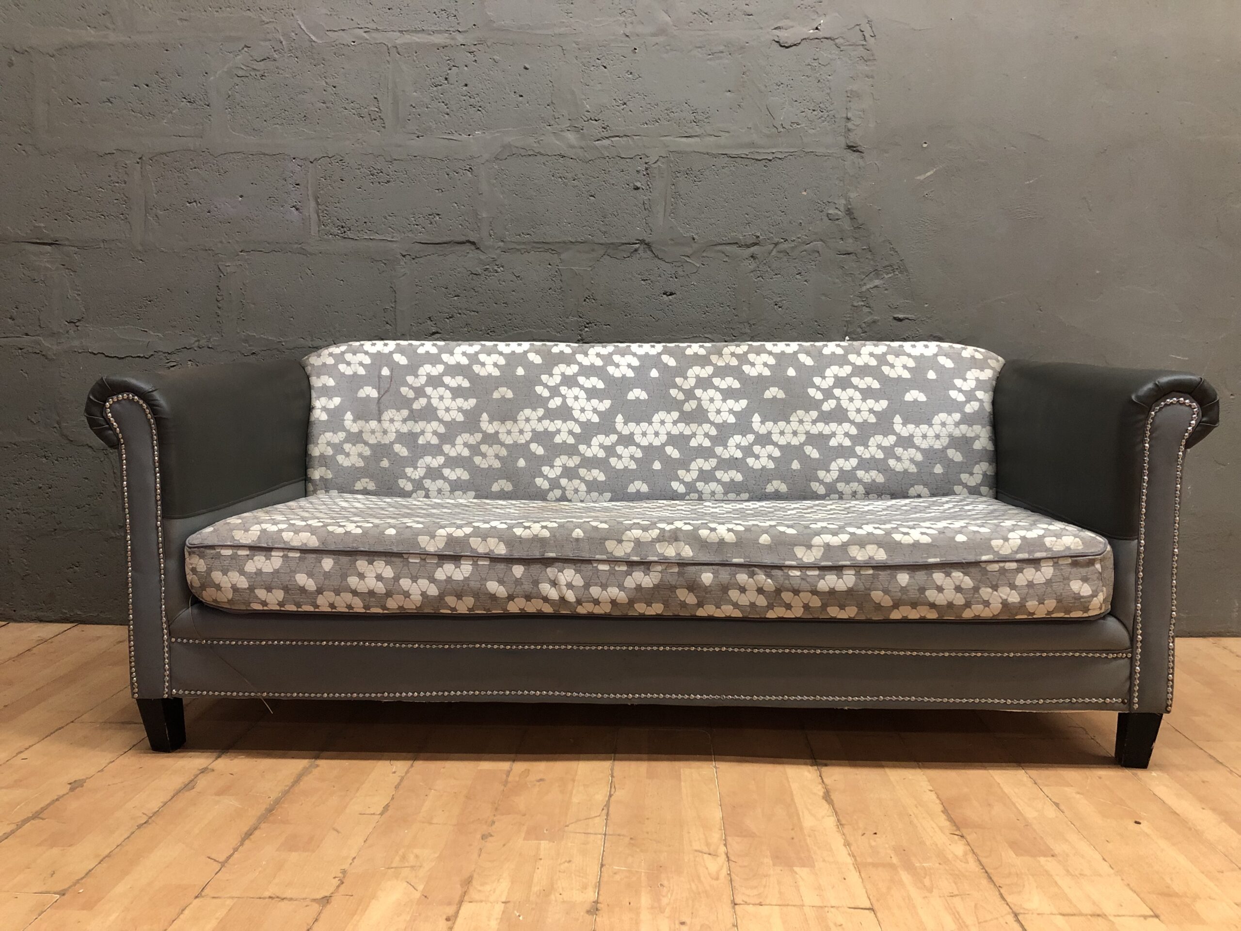 Three-seat patterned grey couch / sofa with visible wear and stains