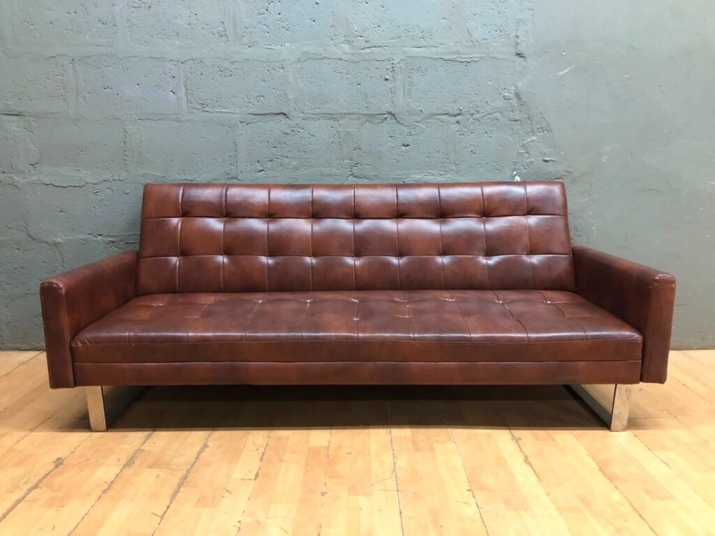 Brown tufted 3‑seater faux‑leather sofa bed with chrome sled legs — converts flat