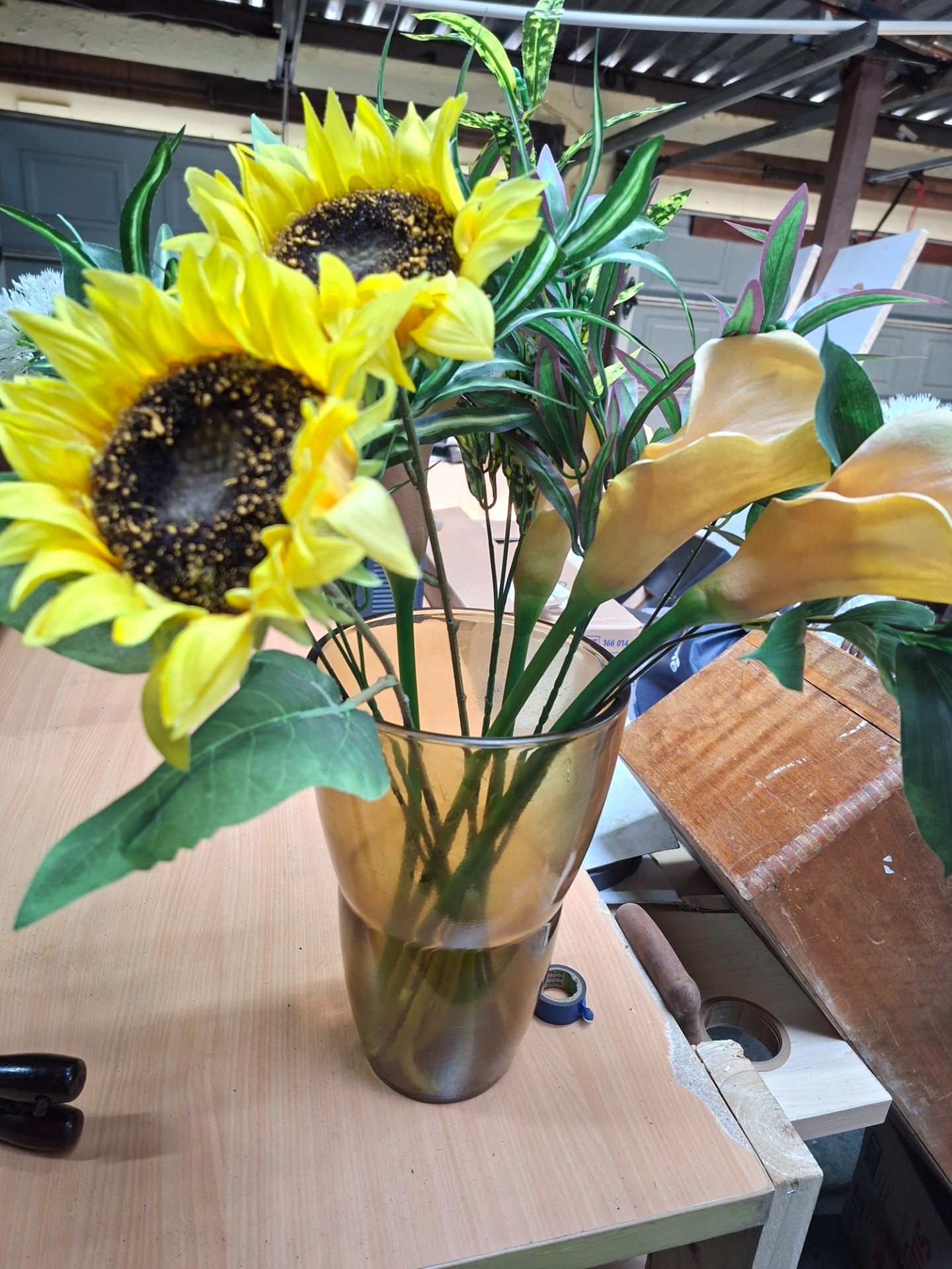 Artificial floral arrangement in amber glass vase ~60cm — mixed sunflowers, calla-style flowers & foliage
