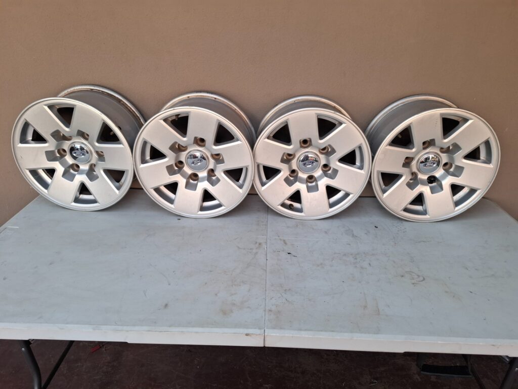Set of 4 Ford alloy wheels (marked 15x7JJ) with Ford centre caps & valve stems — used, curb rash
