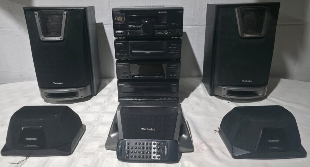 Technics stacked mini hi‑fi system with five speakers and remote — powers on but no volume