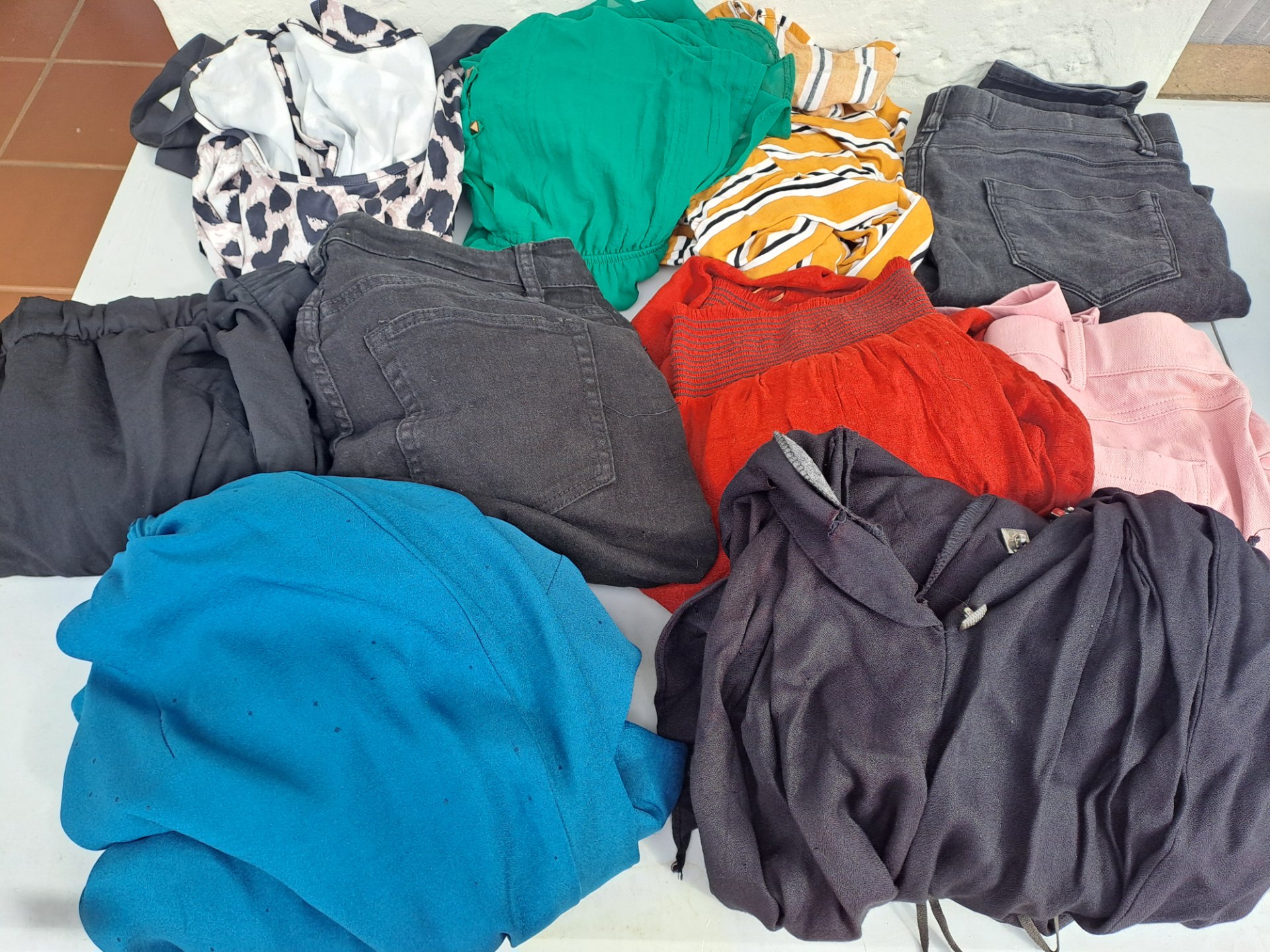 Lot of assorted used clothing — mixed tops, skirts & jeans with visible wear and small stains