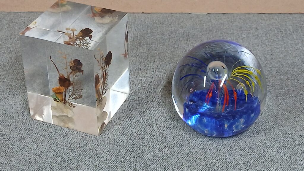 Lot of 2 decorative paperweights — lucite block with dried flowers + round glass paperweight (fair condition, surface scratches)