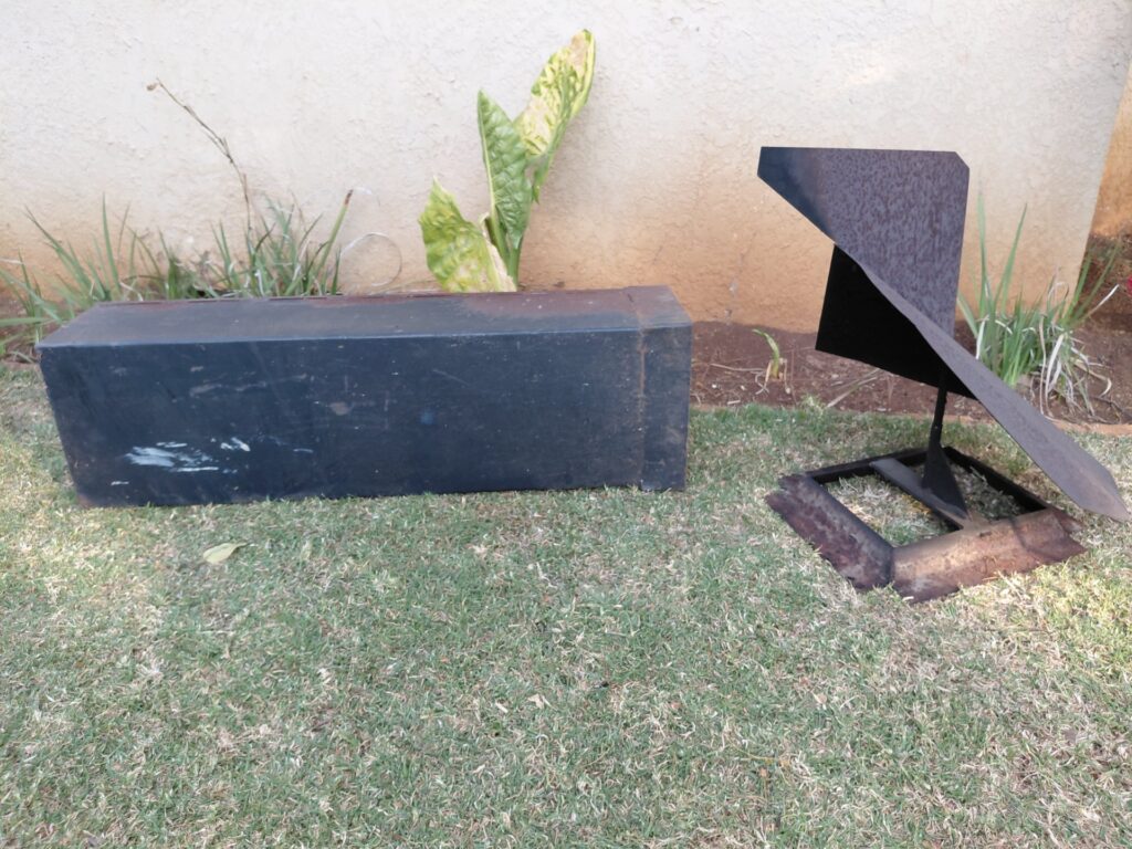 Abstract welded mild-steel garden sculpture with separate rectangular metal box (chimney flue/cowl) — heavy surface rust