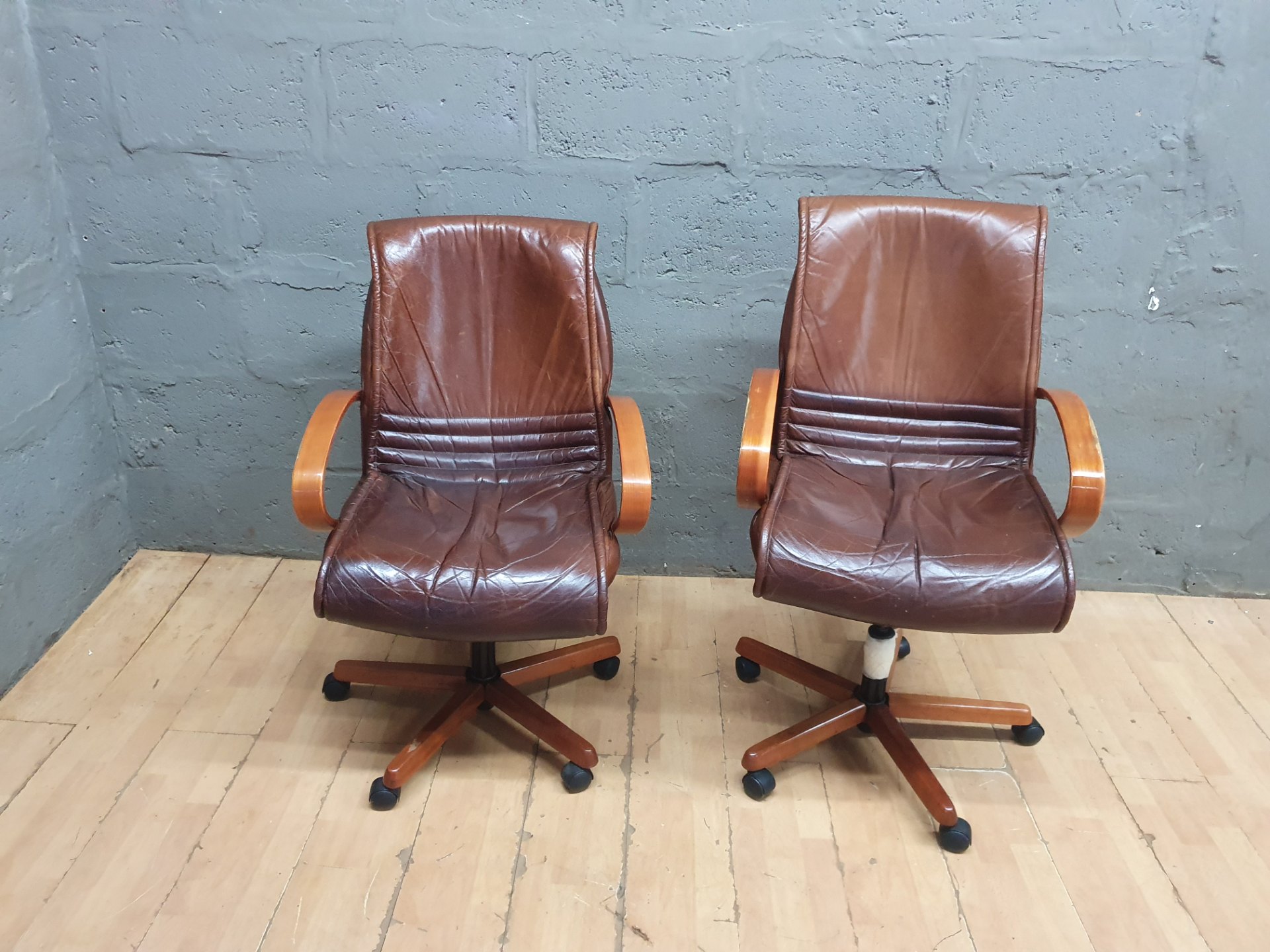 Pair of brown leather swivel office chairs with wooden arms and bases — worn, needs service