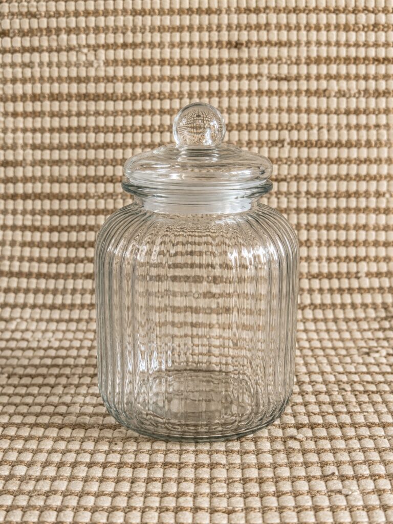 Two ribbed clear glass storage jars with lids + small decorative Roman‑numeral clock (as pictured)