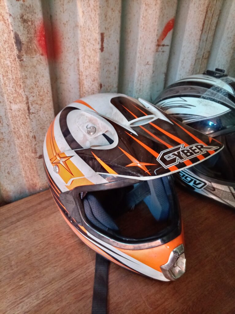 Pair of used off-road/full-face motorcycle helmets (orange ‘CYBER’ + black/white) — heavy wear, one with shell damage — for parts/repair