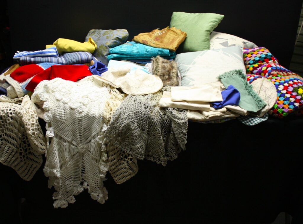 Mixed lot approx 25+ cushions, cushion covers, crocheted throws, doilies & linens — used, staining & fraying visible, sold AS IS