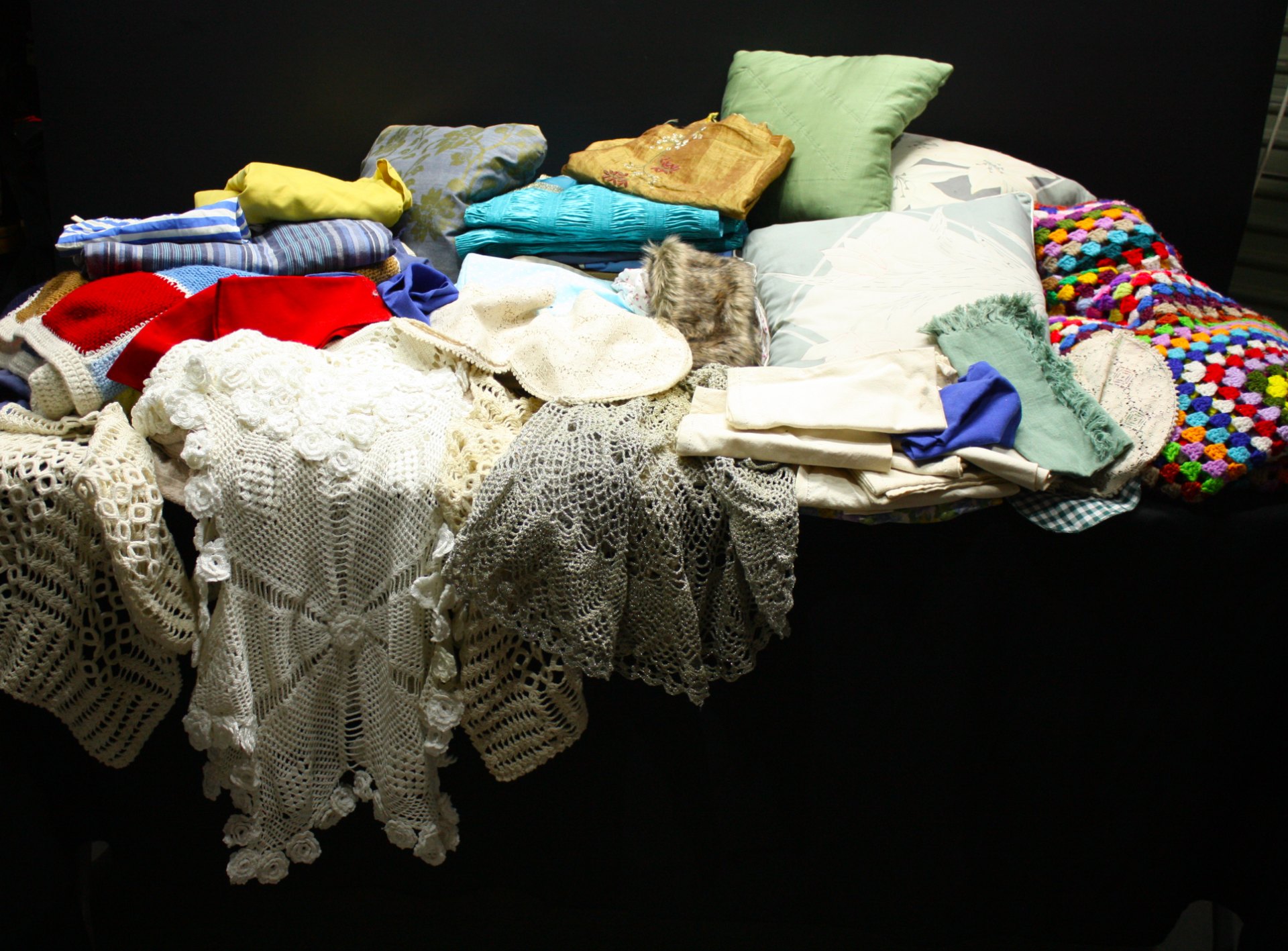 Mixed lot approx 25+ cushions, cushion covers, crocheted throws, doilies & linens — used, staining & fraying visible, sold AS IS