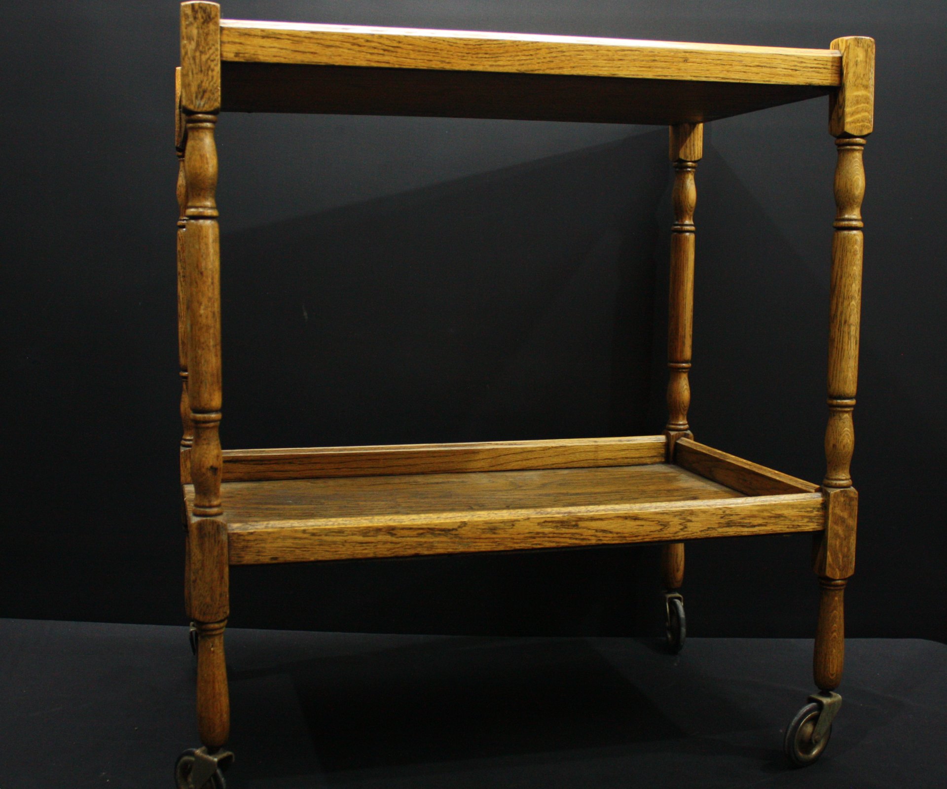 Vintage two-tier wooden serving trolley on swivel castors — turned legs, warm patina
