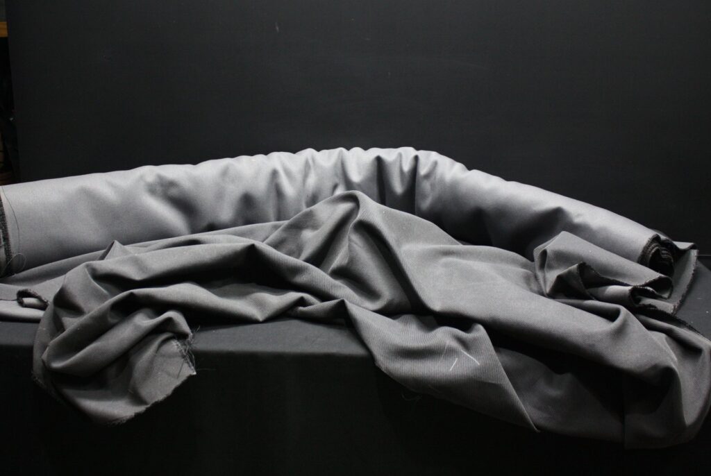 Grey twill-weave fabric bolt — many metres, used roll with clean surface and minor frayed edges