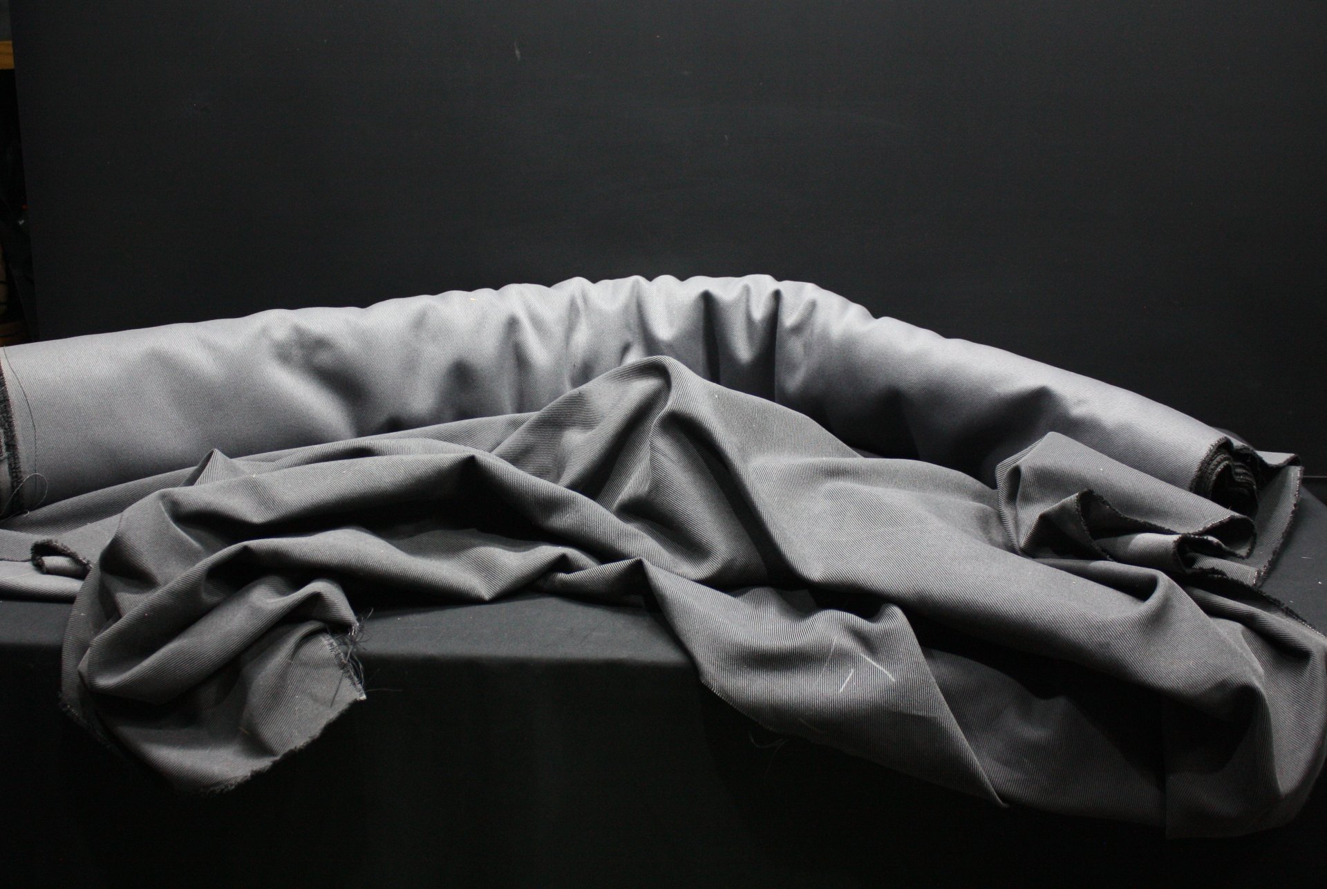 Grey twill-weave fabric bolt — many metres, used roll with clean surface and minor frayed edges