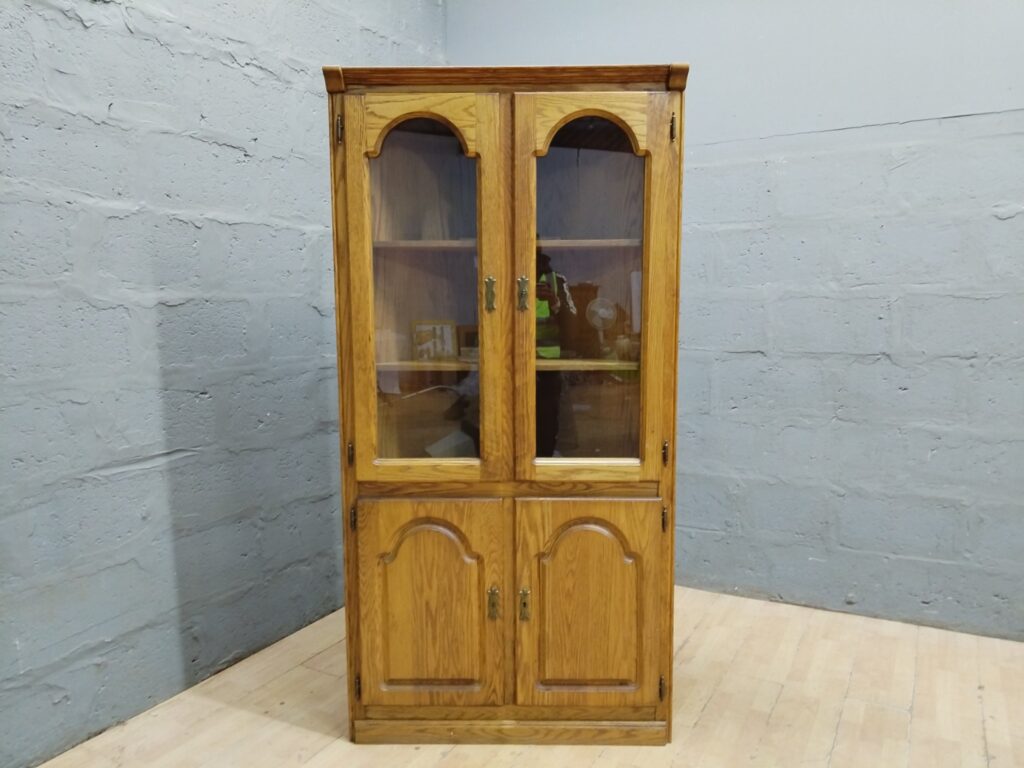 Tall corner display cabinet — glass-front upper doors, lower storage, oak-finish