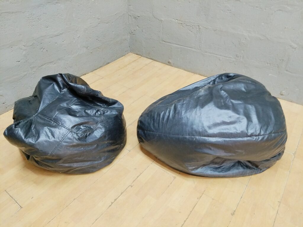 Pair of black faux-leather bean bag chairs — worn covers, flattened filling