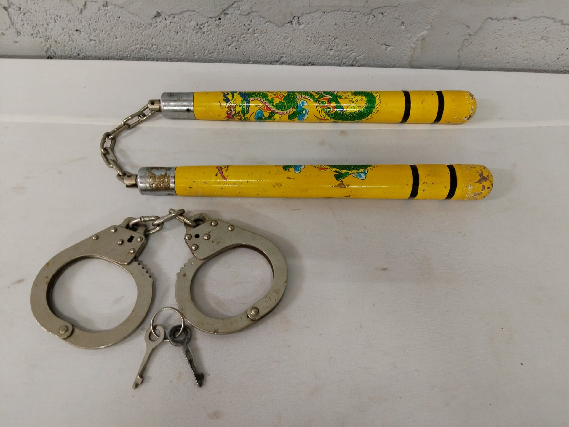 Mixed lot: Hinged metal handcuffs with two keys + yellow dragon-decorated nunchaku