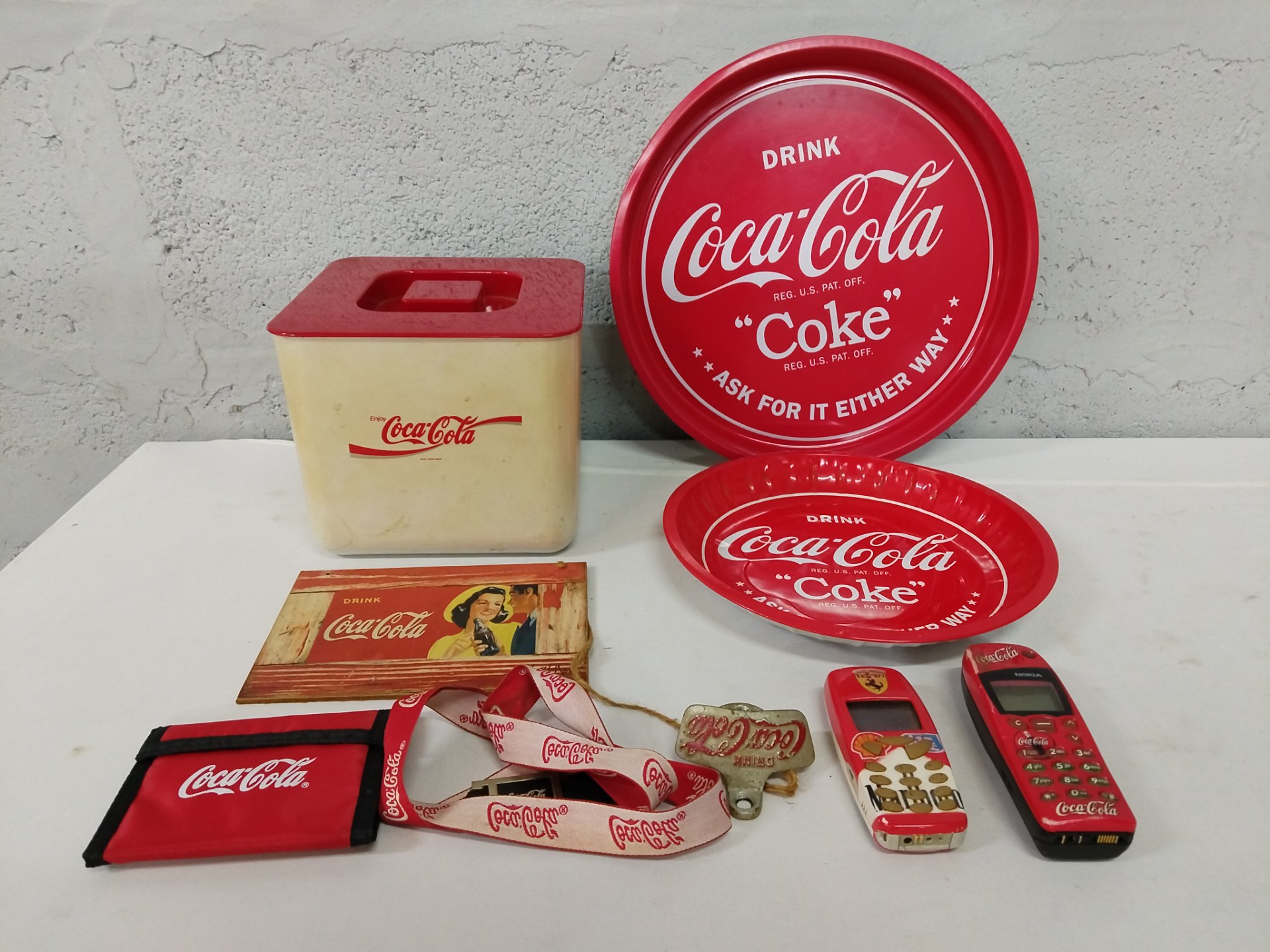 Lot of 9 Coca‑Cola promotional items — trays, plastic container, wooden plaque, lanyard, opener, pouch & 2 novelty phones (phones not working)