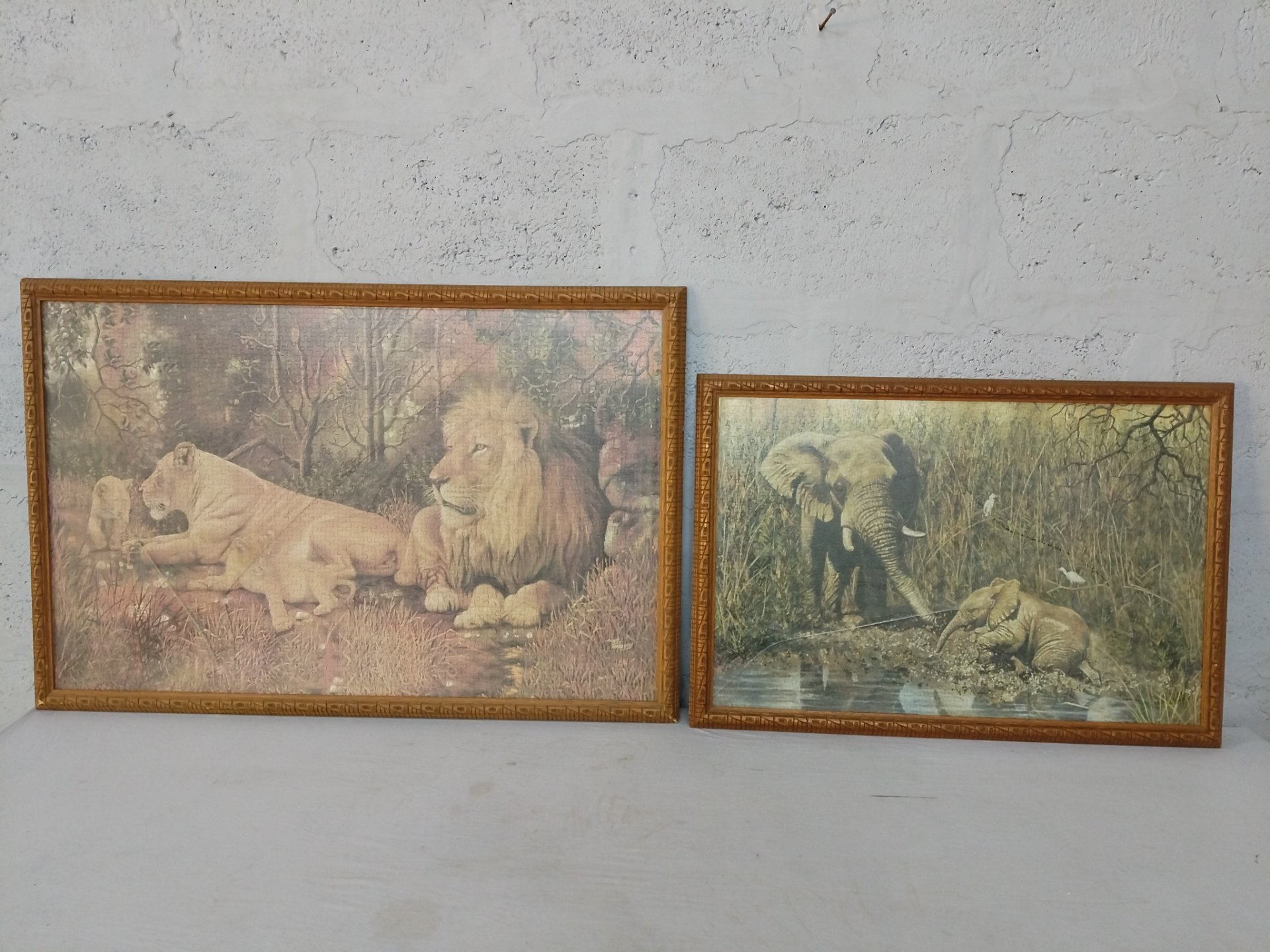 Pair of framed completed jigsaw puzzles — lion and elephant scenes, carved wooden frames (sizes 96×63 cm & 75×52 cm)