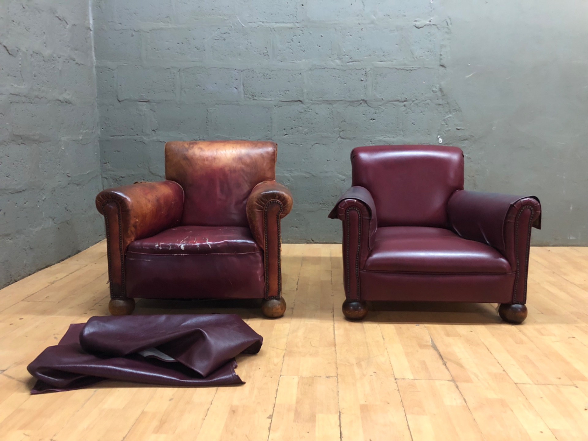 Pair of leather club armchairs — one heavily worn, one good, loose leather covers included