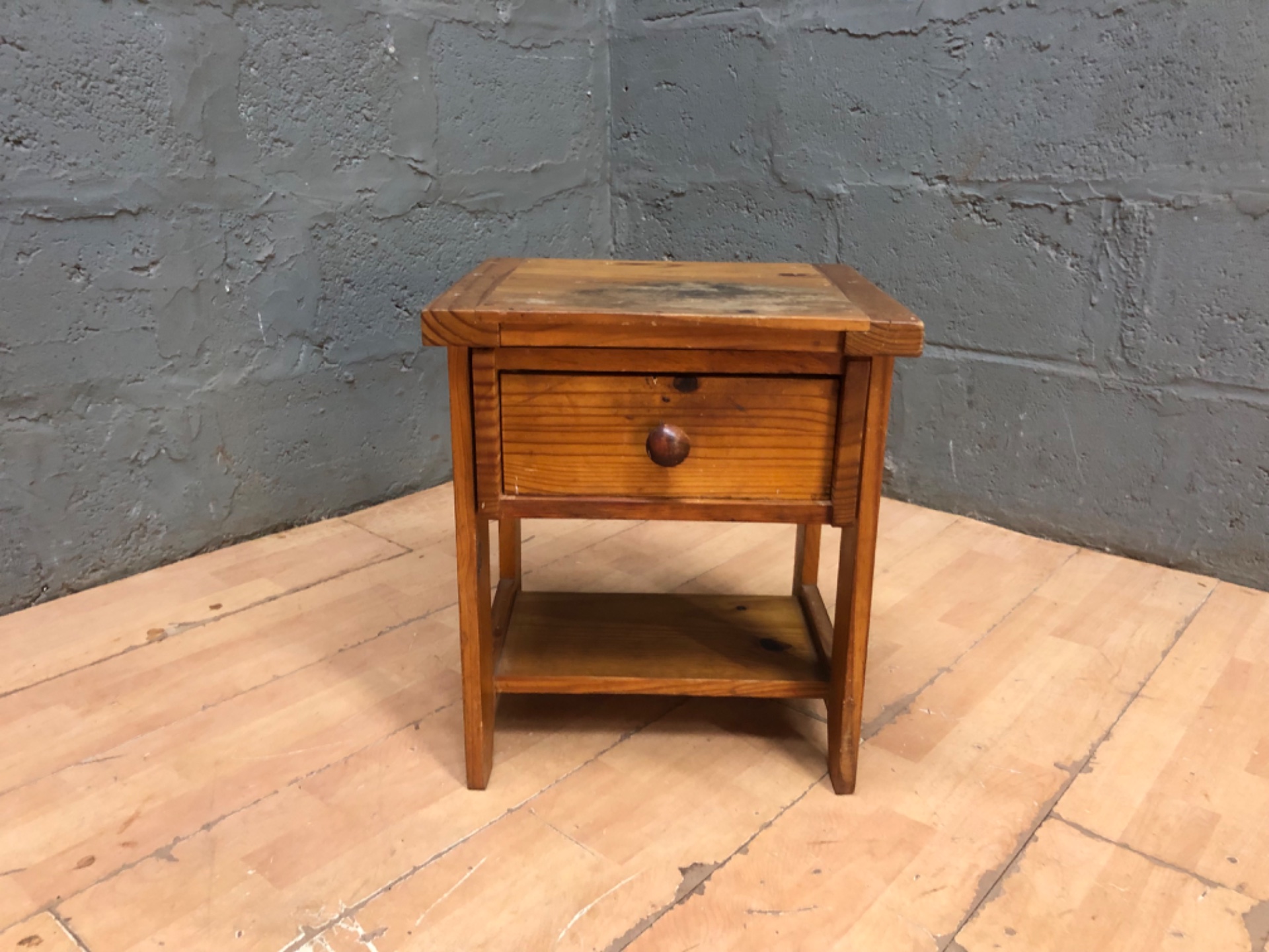 Small solid-wood bedside / side table with single drawer and lower shelf — worn, stained top