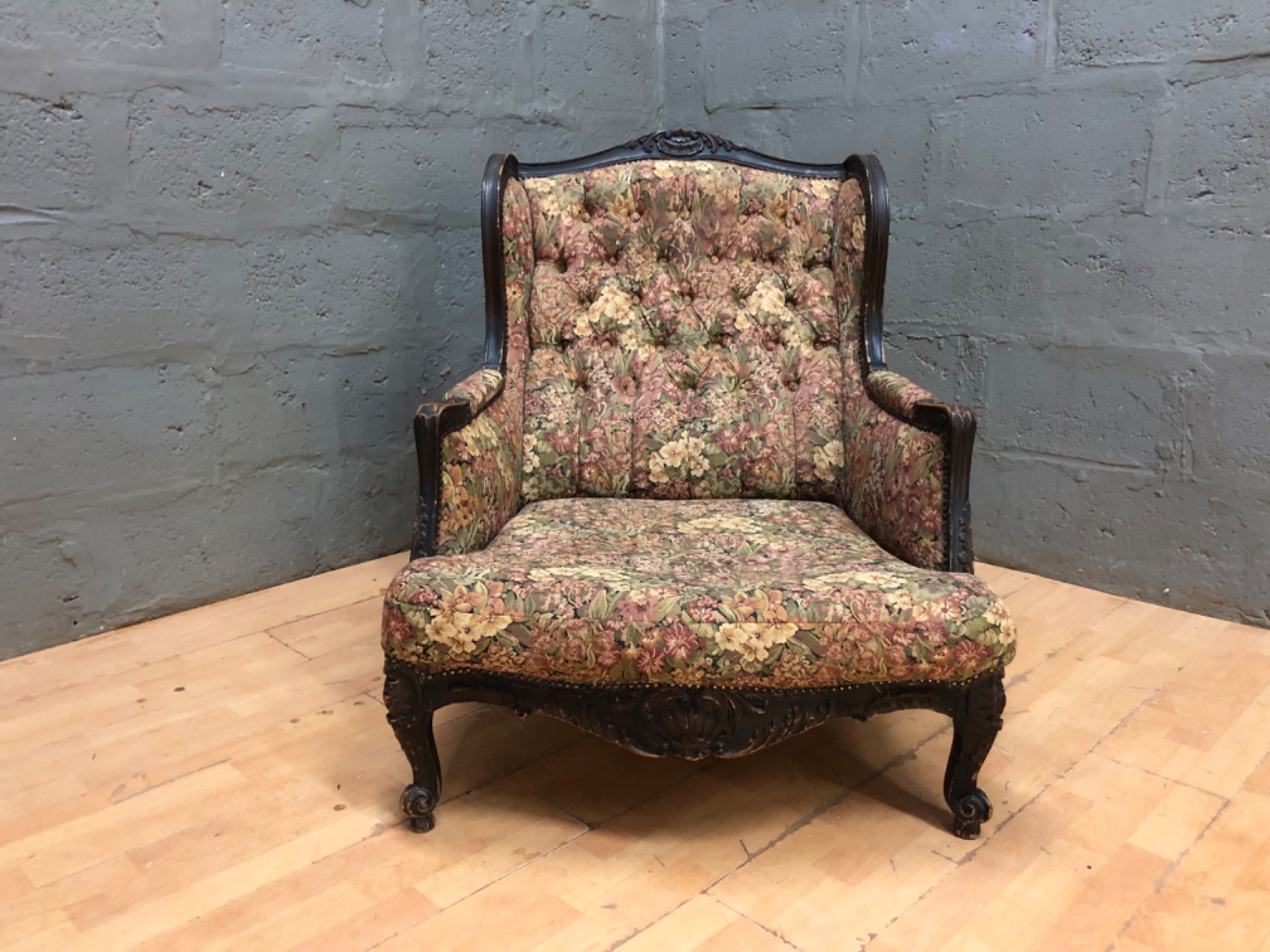 Vintage tufted wingback armchair with carved wooden frame and floral tapestry upholstery