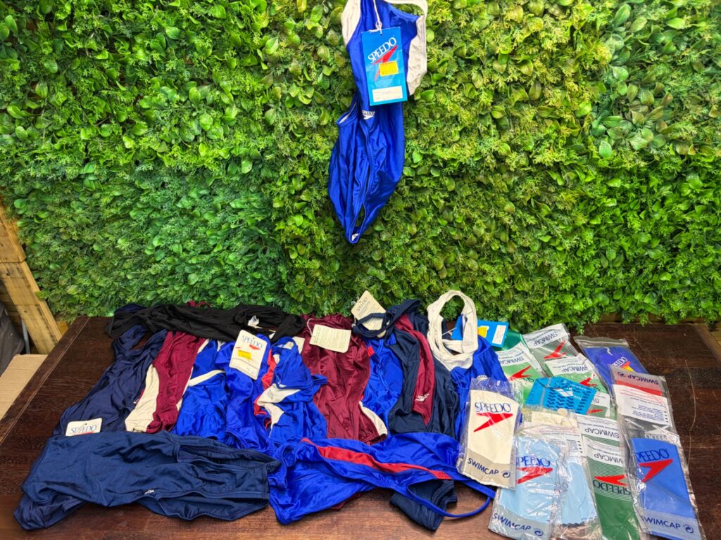 Bulk lot of Speedo one‑piece swimsuits + sealed Speedo swim caps — mixed/new tags visible
