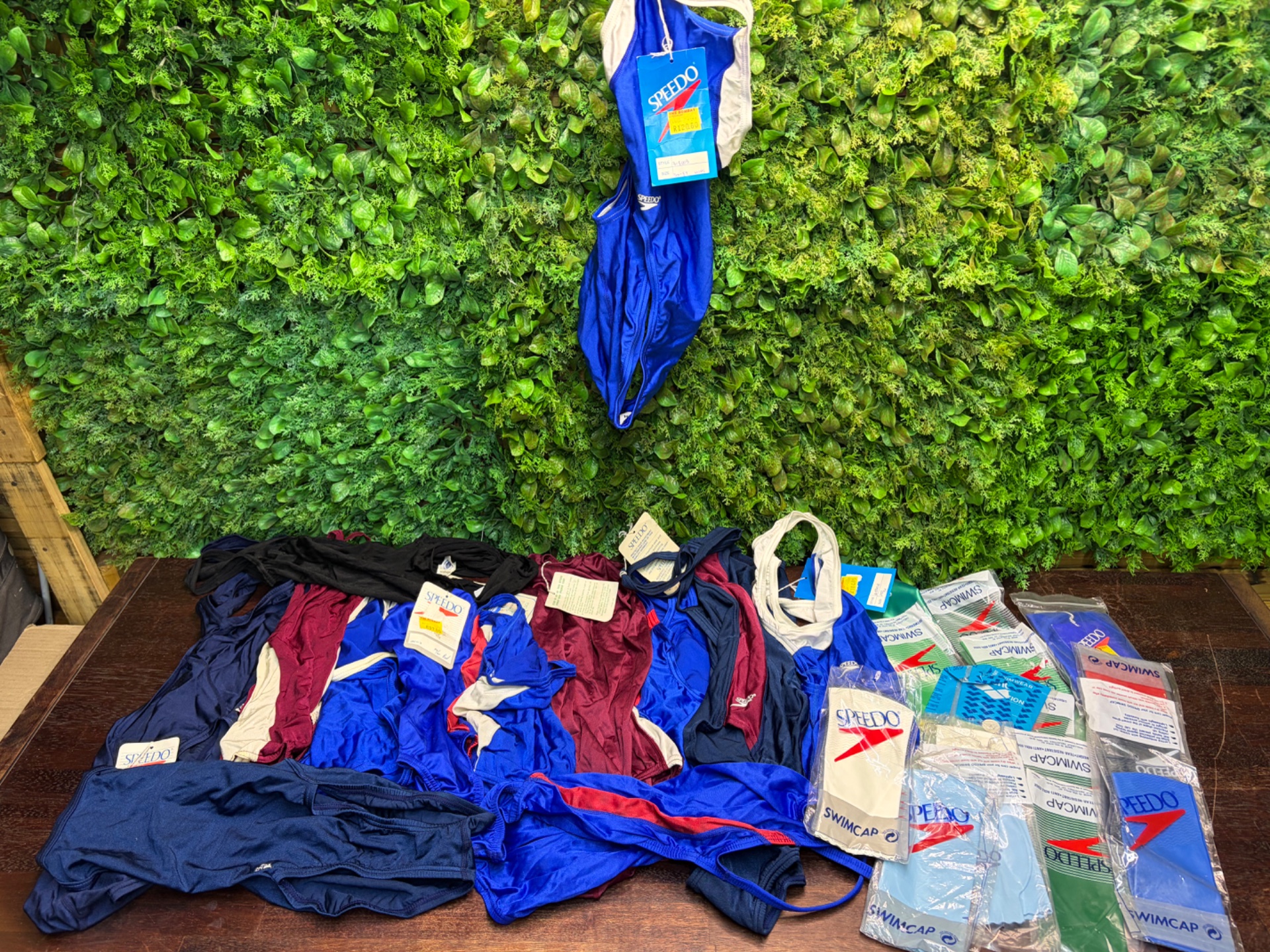 Bulk lot of Speedo one‑piece swimsuits + sealed Speedo swim caps — mixed/new tags visible