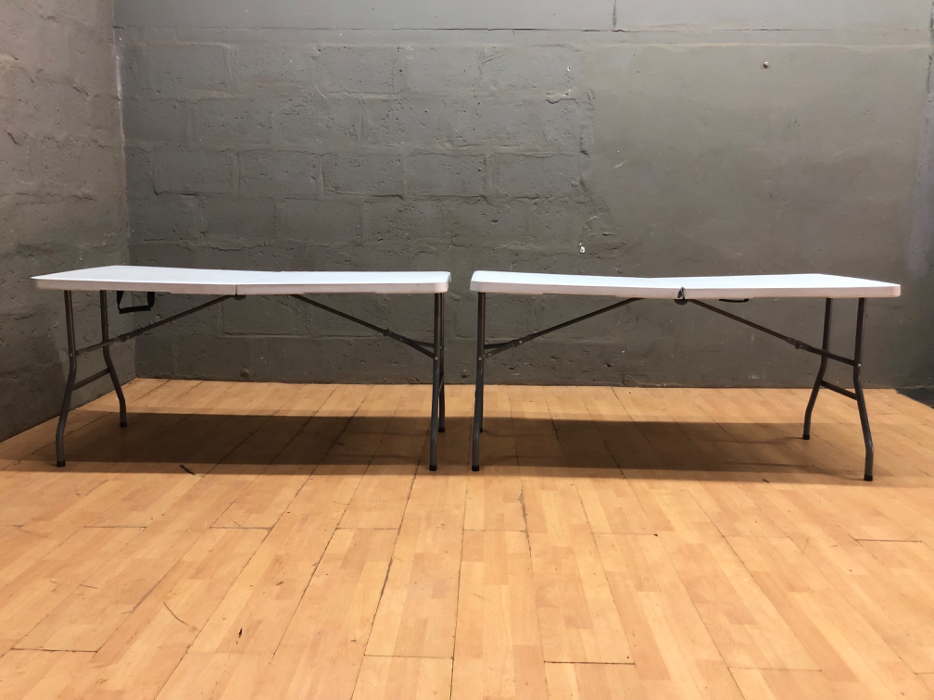 Pair of white folding plastic banquet tables — 153 x 71 x 74 cm each, one with split at centre seam
