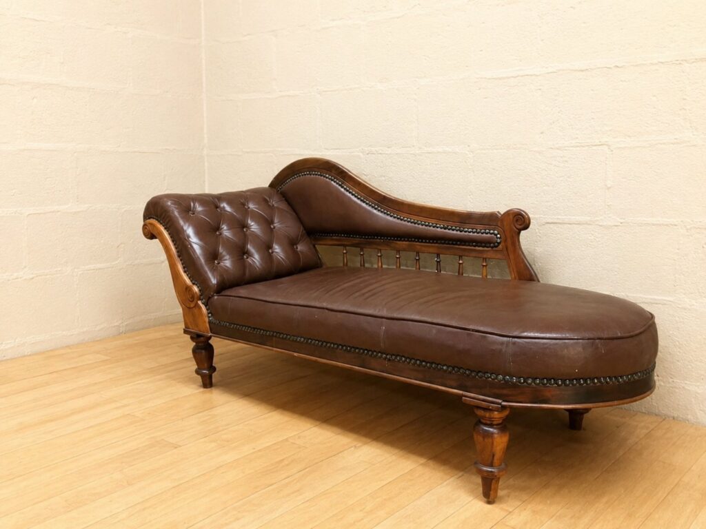 Brown tufted leather chaise longue on carved wooden frame — nameplate ‘Jonker Stinkhout, Knysna’