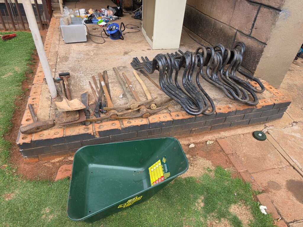 Mixed job lot: 29 garden/hand tools + 12 black curved metal frames, 2 wheelbarrow frames & Lasher wheelbarrow tub (tub missing wheel/handles)