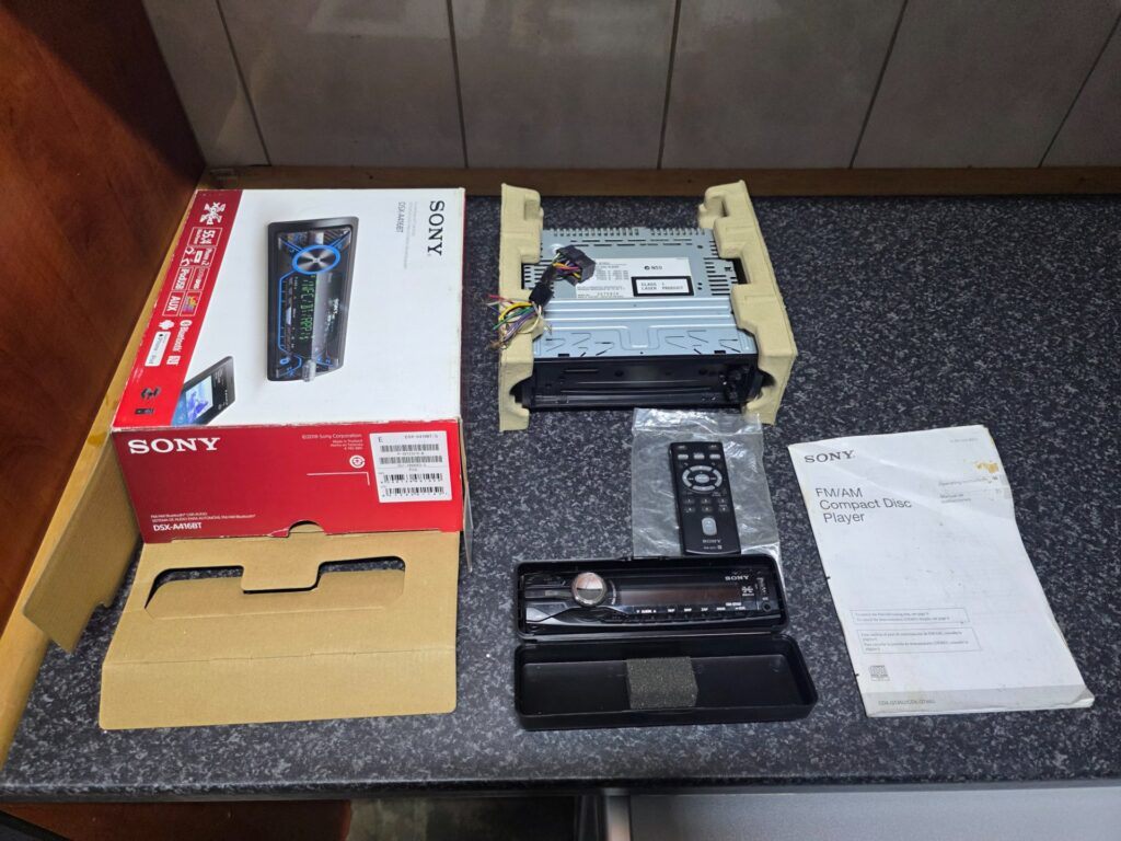 Sony single‑DIN car stereo head unit with detachable face, remote, manual, wiring & box