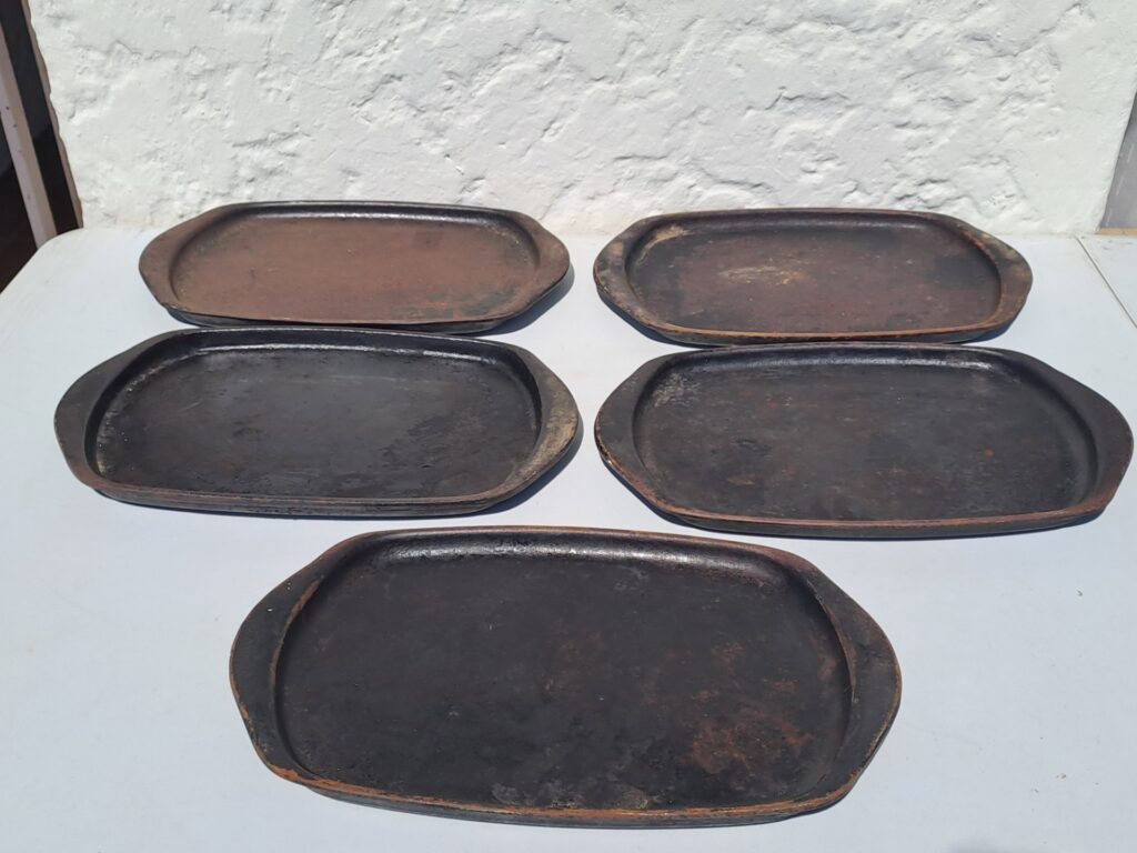 Set of oval cast-iron sizzle / serving plates (five shown) — heavy rust & pitting, maker stamp ’18B’ visible