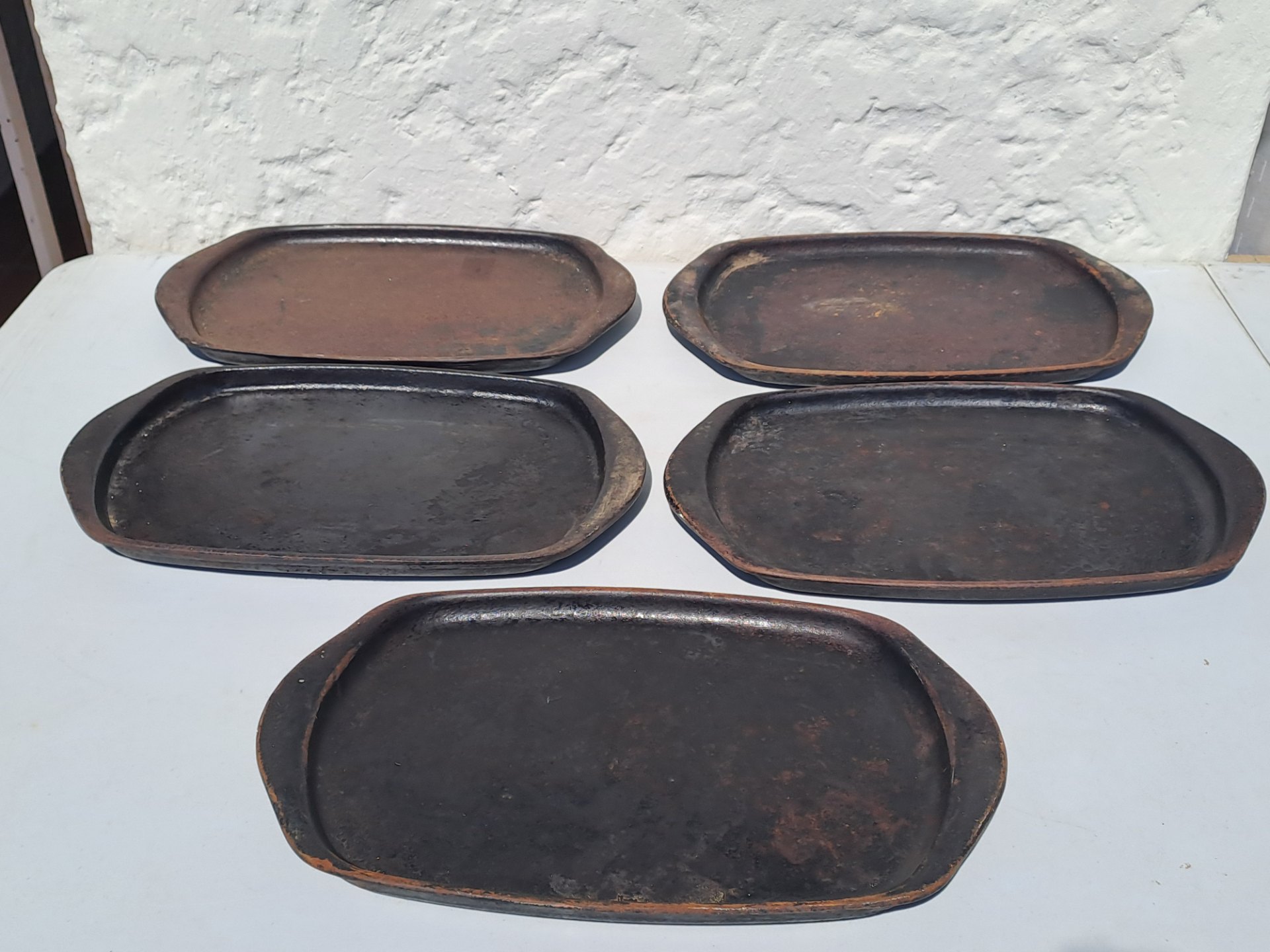 Set of oval cast-iron sizzle / serving plates (five shown) — heavy rust & pitting, maker stamp ’18B’ visible