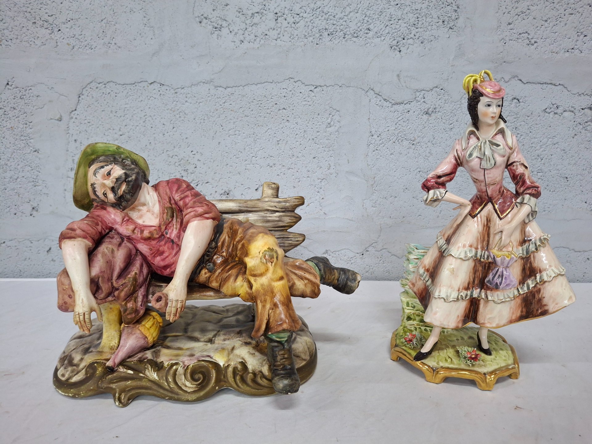 Pair of decorative porcelain figures — reclining man on bench & standing lady (one marked Capodimonte)