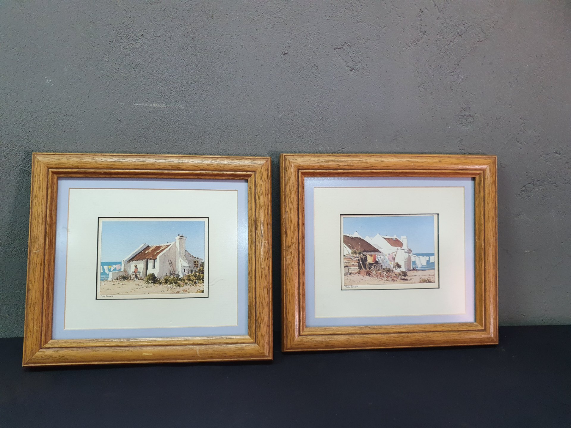Pair of matted coastal prints in oak-effect frames (signed, sold as pair)