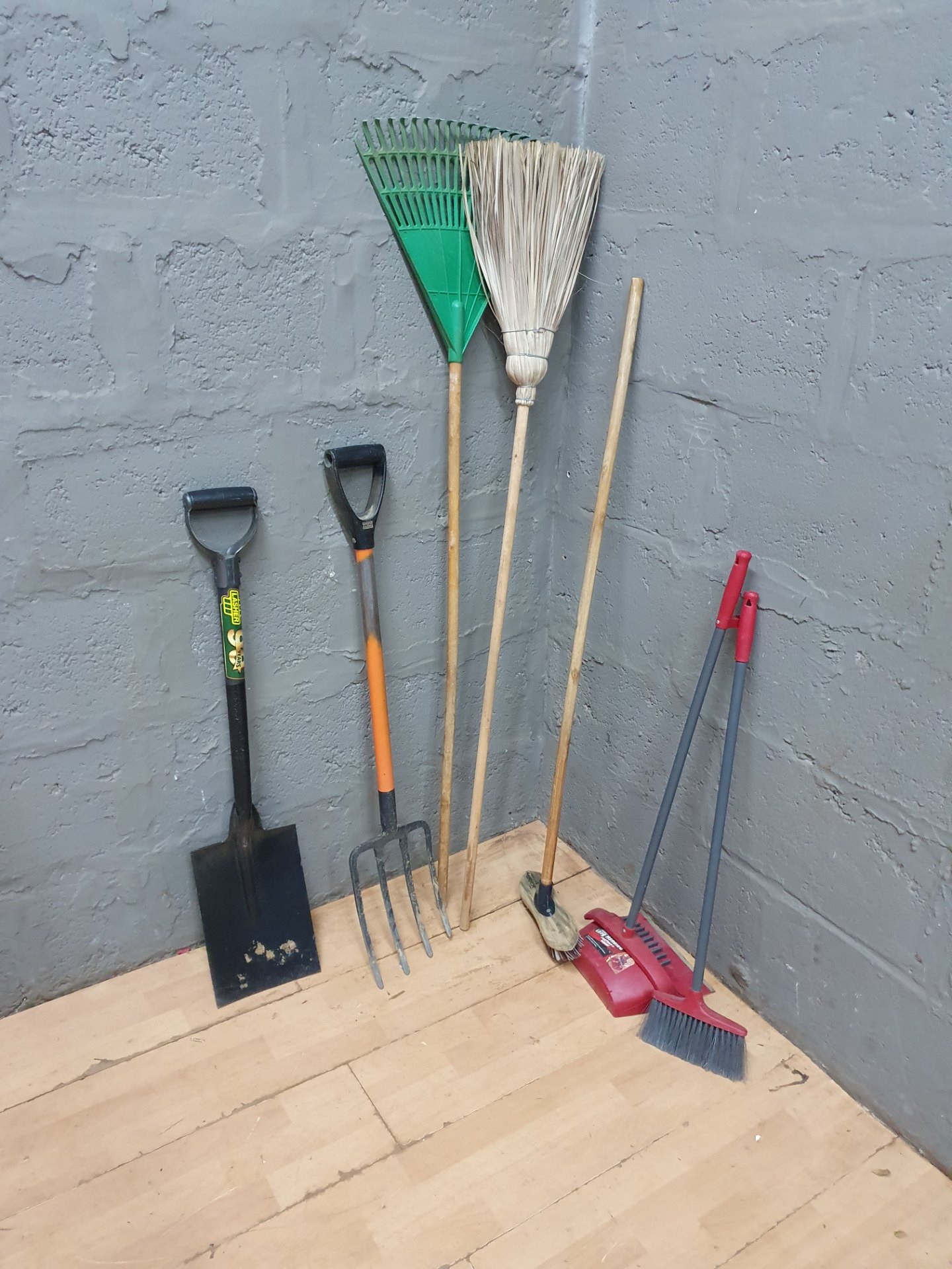 Mixed lot of 7 garden hand tools — shovel, 4-tine fork (damaged), rakes, brooms, dustpan and spare handles
