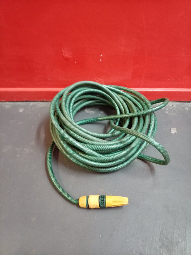 Used green reinforced garden hose with yellow quick‑connect nozzle — one end frayed, untested