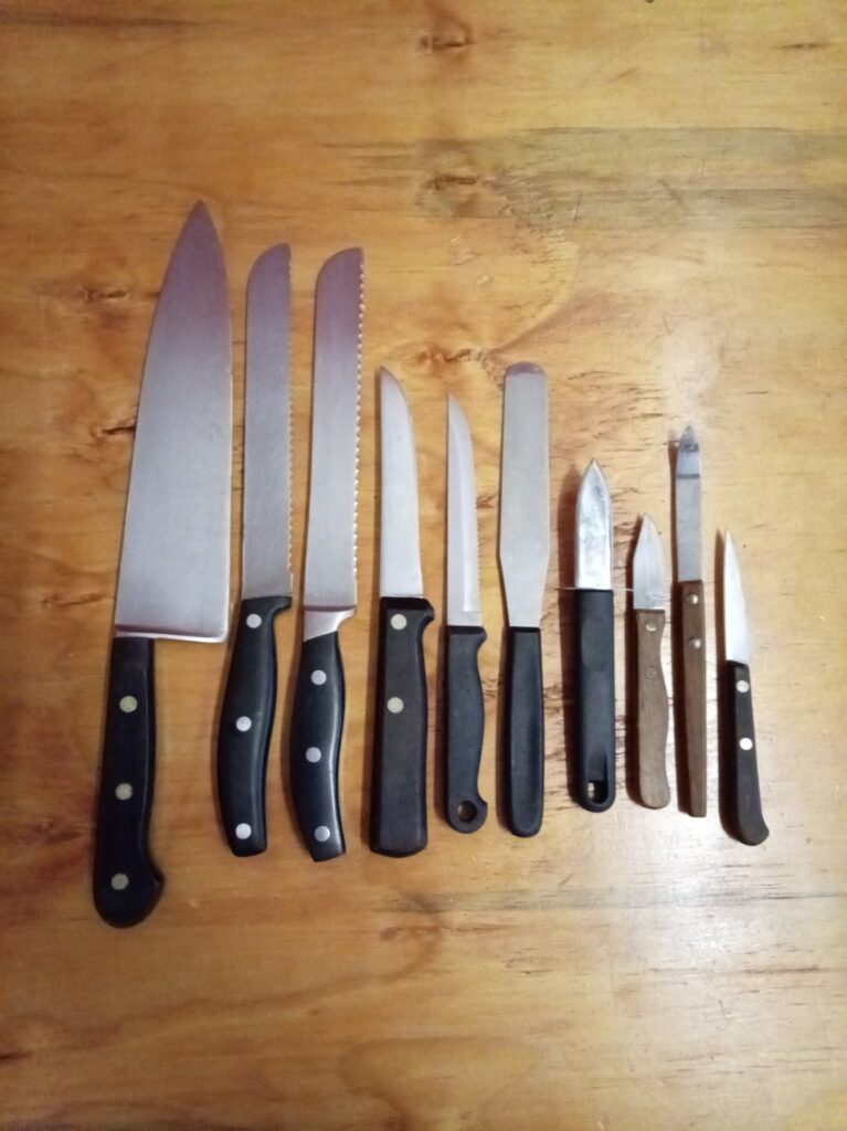 Assorted kitchen knife lot (approx. 9–11 pieces) — large chef, serrated blades, paring knives & spreader, used with staining and some rust