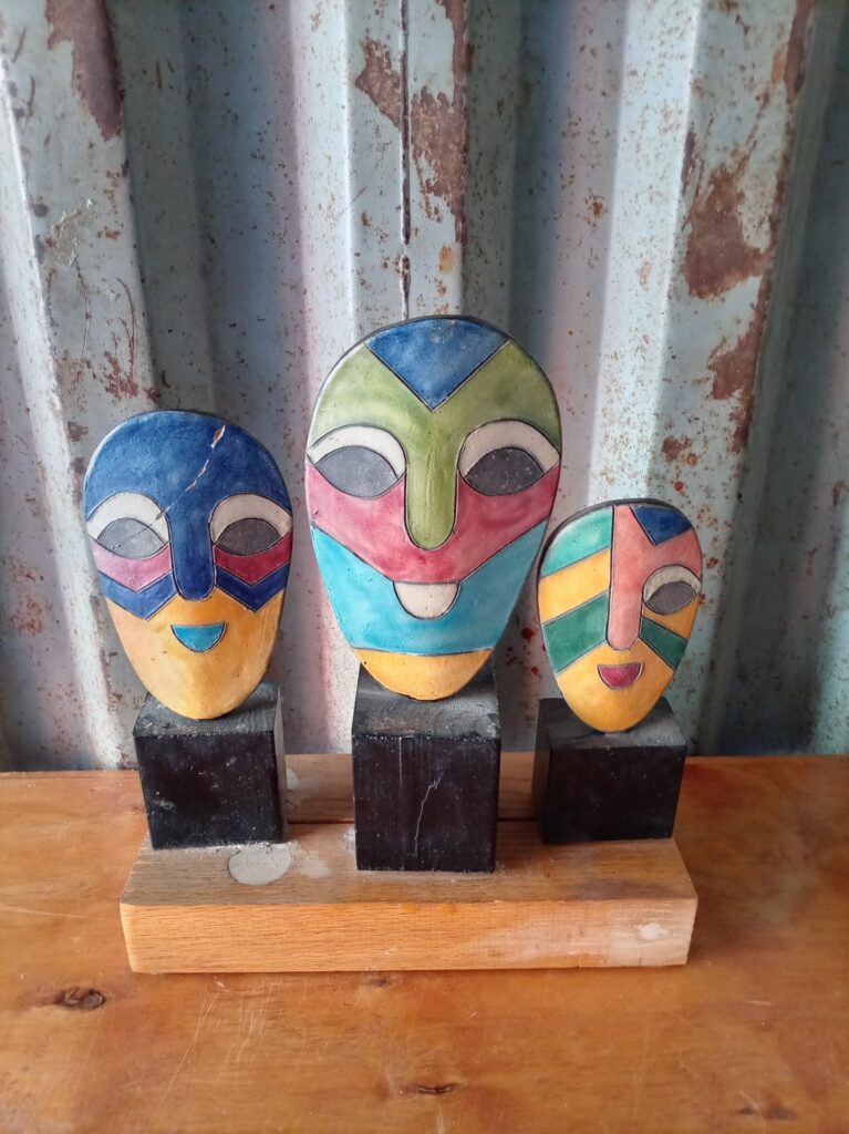 Set of three colourful painted mask sculptures on wooden base