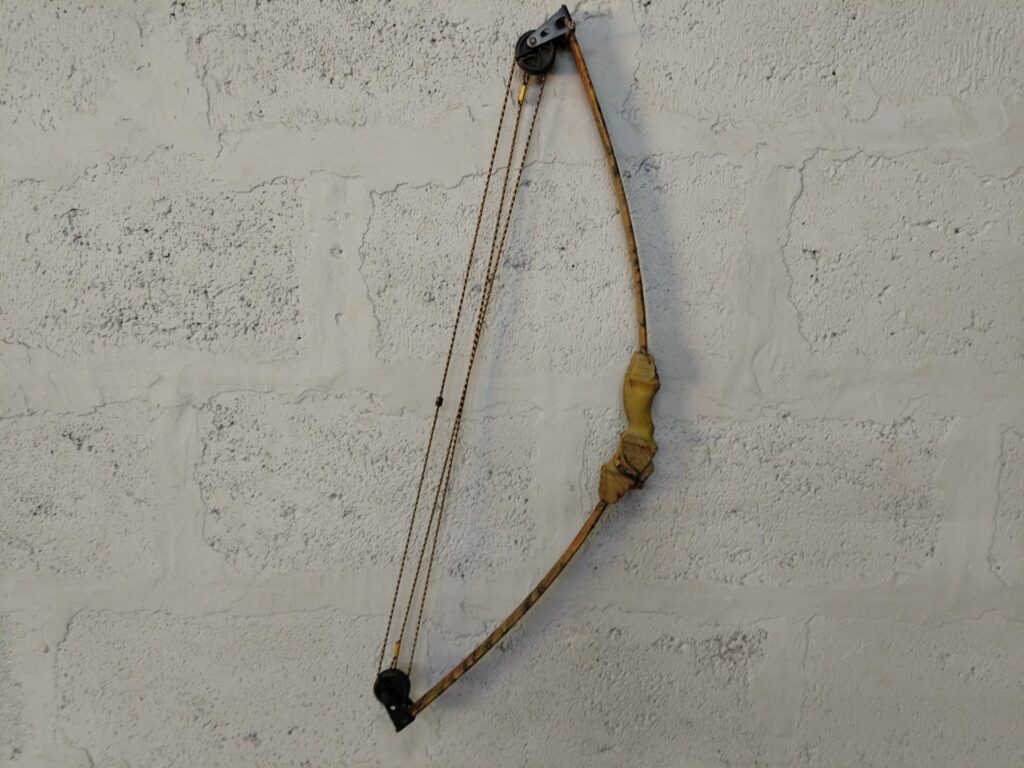 Cam-style compound bow — camo finish, cam/pulley system, strings present (64 cm tip-to-tip)