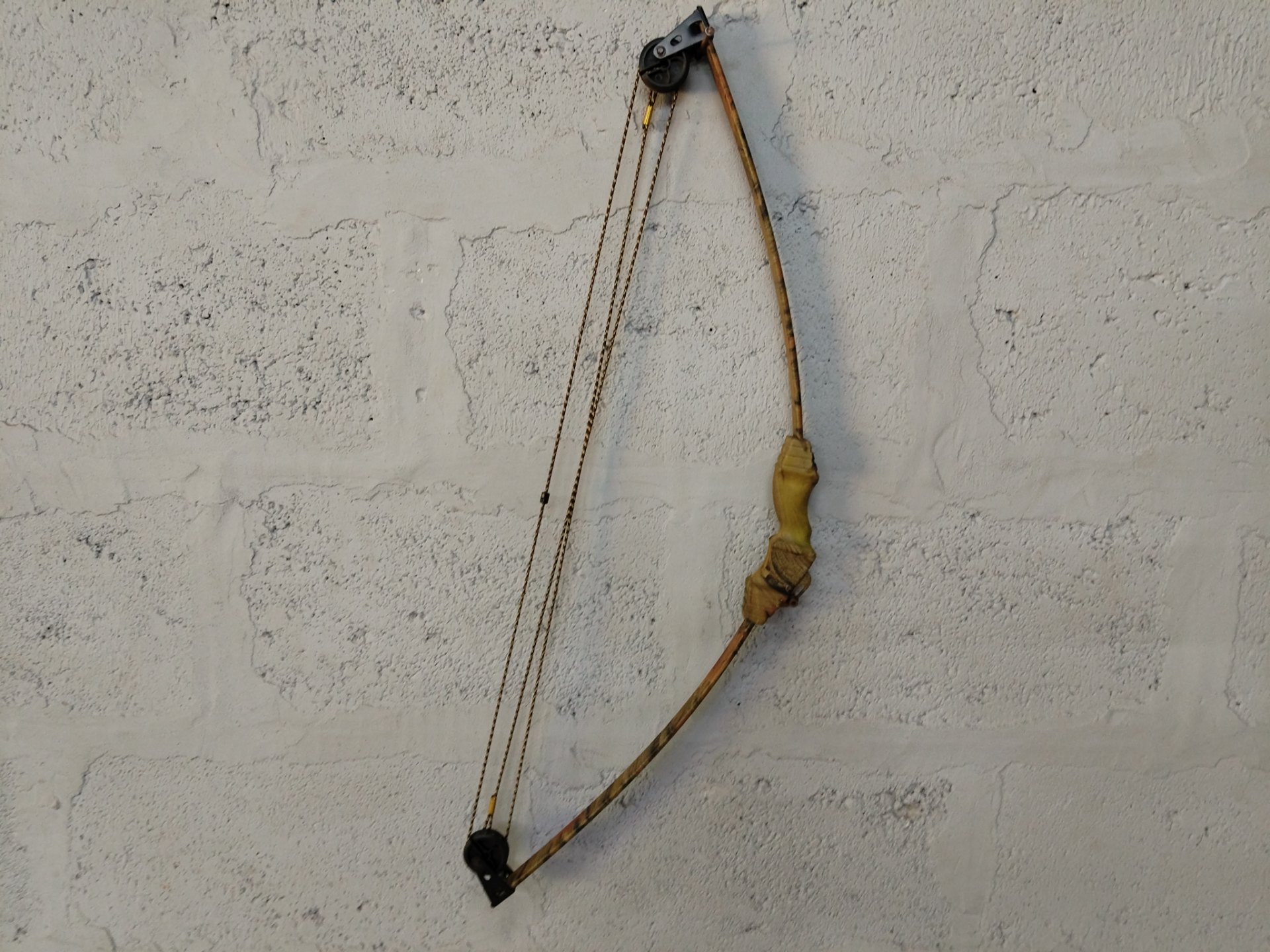Cam-style compound bow — camo finish, cam/pulley system, strings present (64 cm tip-to-tip)