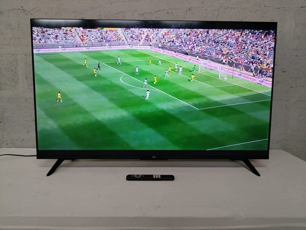 TCL flat-screen TV (111 x 69 cm) — powered on in photos, remote & power cable included