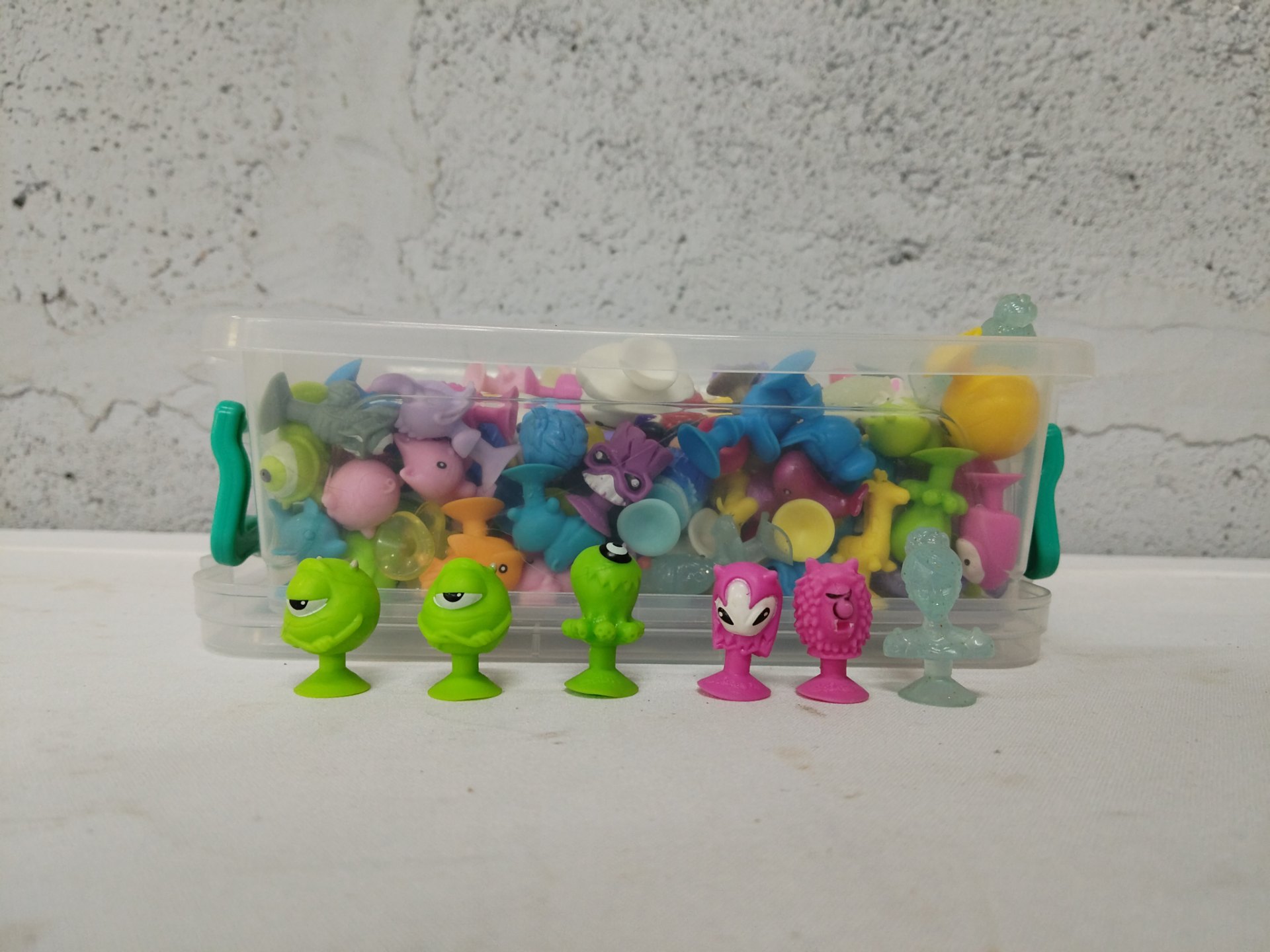 Bulk lot — ~60 assorted small suction‑cup toy figures in clear lidded storage box