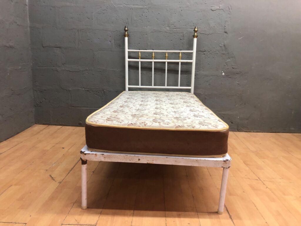 Single Metal Bed Frame with Mattress — White frame, brass finials, solid base