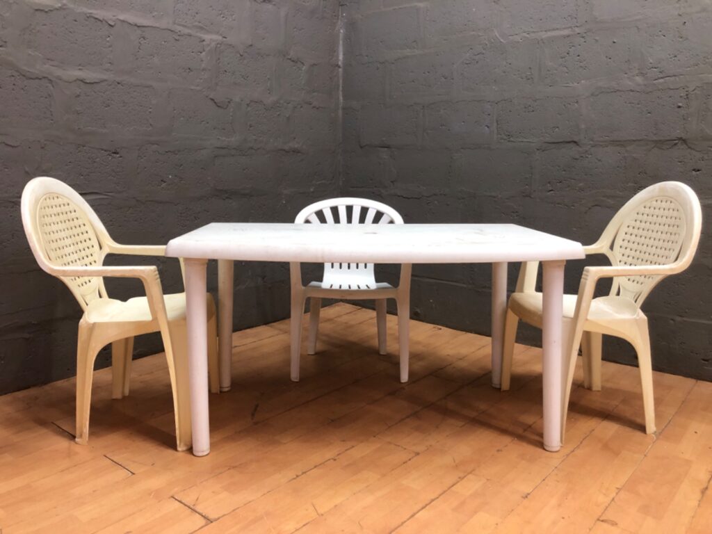 Used plastic outdoor table (131 x 82 x 71 cm) with 3 plastic chairs – heavy cosmetic wear, sold as-is