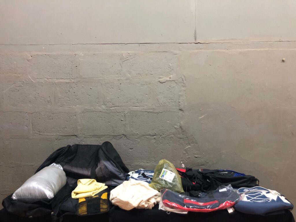 Mixed lot — 14 backpacks, bags, clothing & accessories (logos visible: MSC, Billabong, Ferrari, Guess)