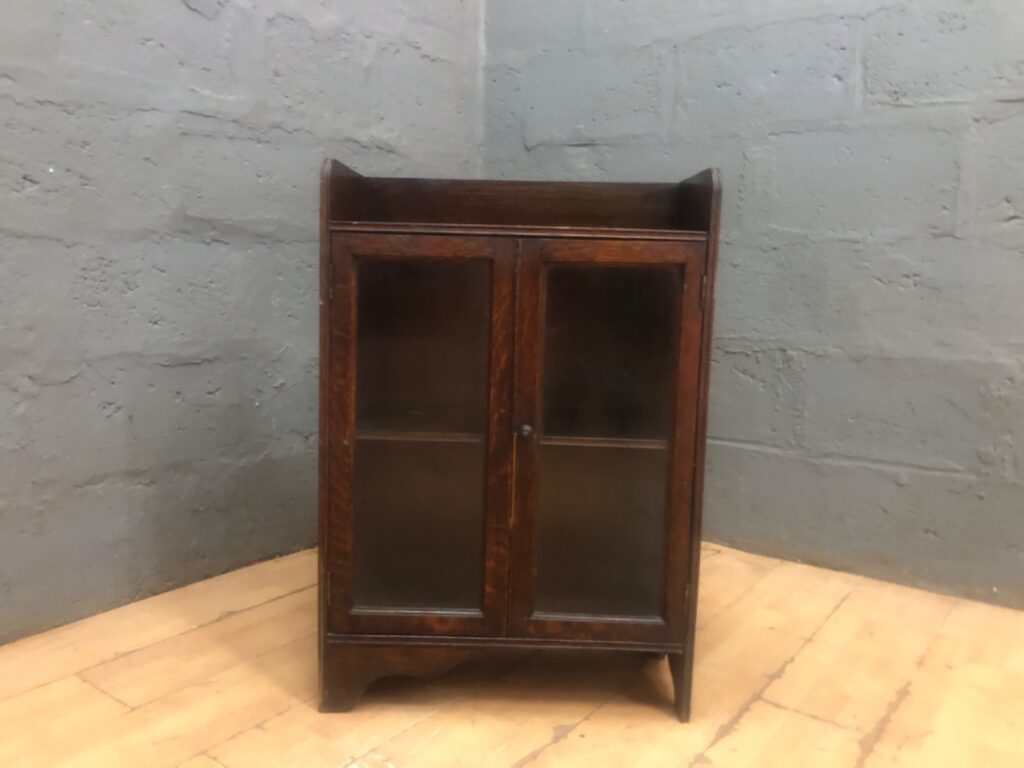 Small oak‑tone glazed display cabinet – two doors, fixed shelf, raised top tray