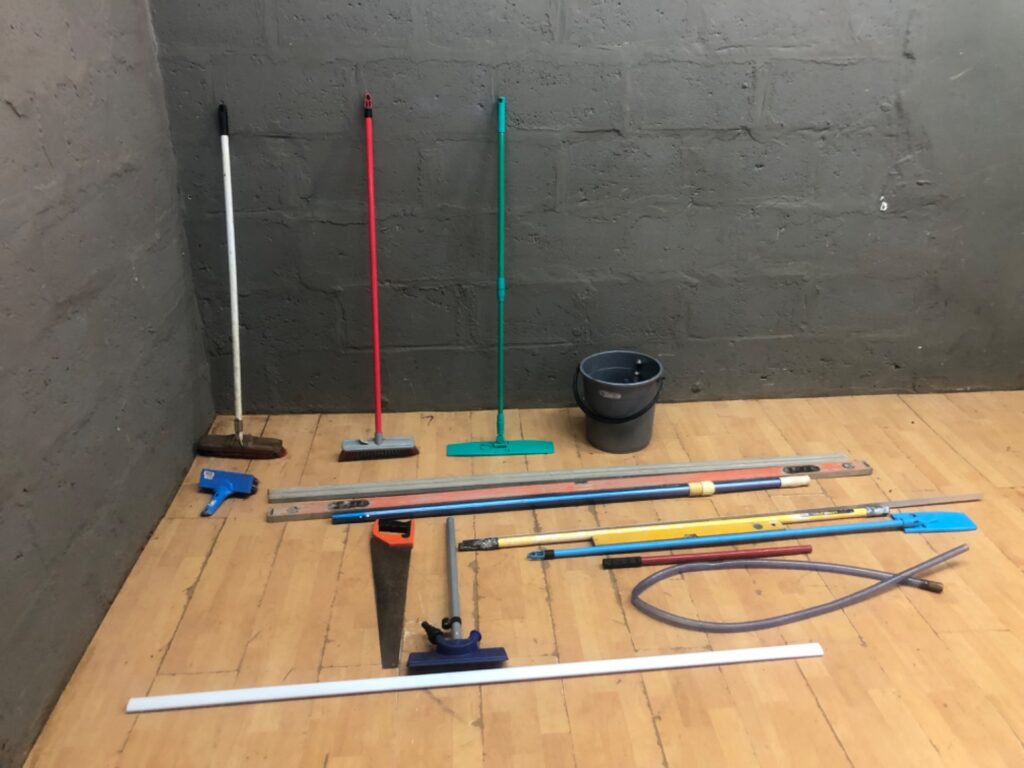 Lot: 17x Used Cleaning Tools & Pole Implements — Brooms, Squeegees, Bucket, Levels, Hose, Hand Saw (blade exposed)