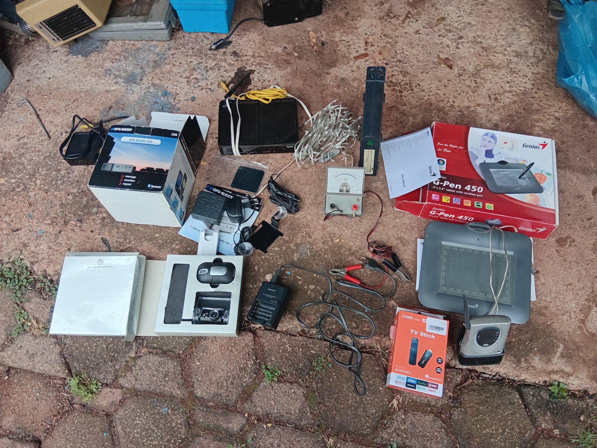 Mixed small electronics lot — Genius G‑Pen 450 tablet, GPS‑Buddy units, ZyXEL router, TV stick, Sony charger, voltmeter & assorted cables (untested)