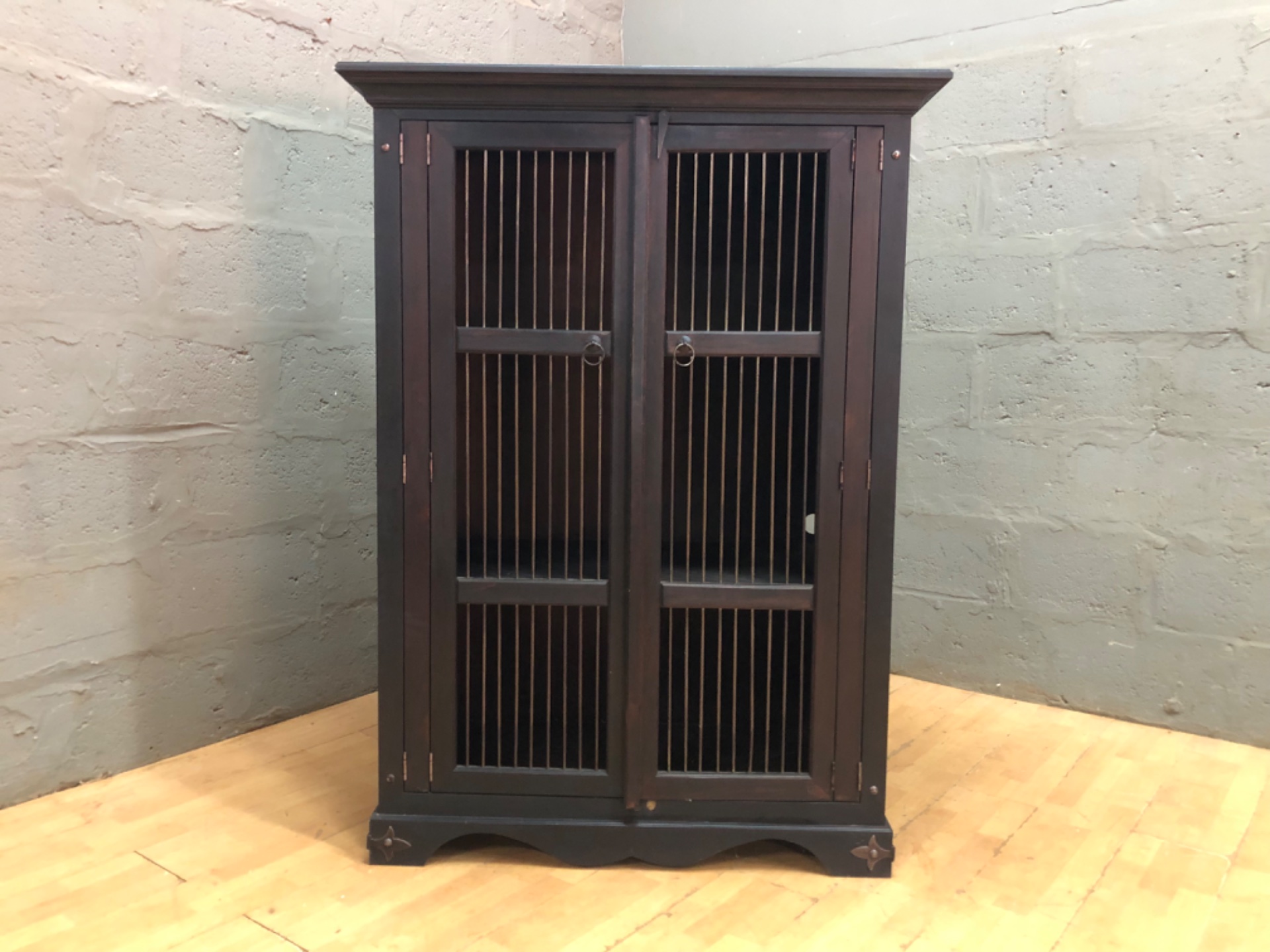 Tall dark-stained wooden freestanding cabinet — barred double doors, fixed shelves, cable hole